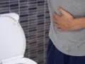 Mężczyzna trzyma się za brzuch, siedząc obok toalety. Może to być jeden z objawów raka odbytu.