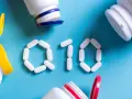 Białe tabletki ułożone w kształt "Q10" na niebieskim tle, obok otwarte pojemniki z suplementami. Koenzym Q10 na co?