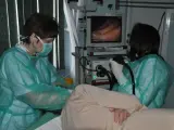 Lekarze w zielonych fartuchach przygotowują pacjenta do gastroskopii, obserwując obraz na monitorze.