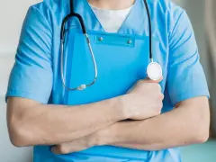 Lekarz rodzinny w niebieskim kitlu trzyma teczkę i stetoskop. Zastanawiasz się, ile zarabia lekarz rodzinny?