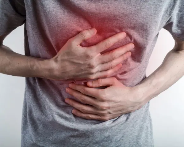 Osoba trzyma się za brzuch, odczuwając ostry ból w klatce piersiowej na środku. Czerwony obszar na koszulce sugeruje miejsce dolegliwości.