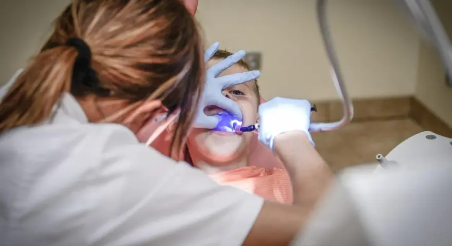 Dentysta w rękawiczkach bada zęby dziecka przy użyciu niebieskiego światła.