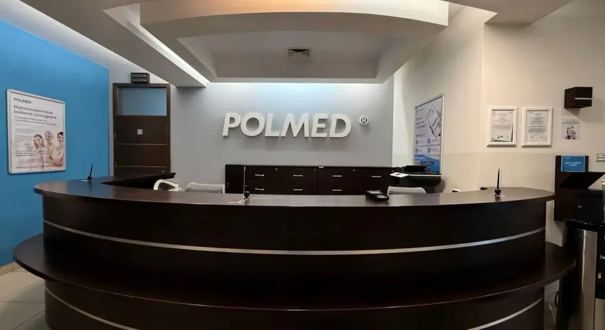 Recepcja kliniki medycznej POLMED z ciemnobrązowym ladą i logo na ścianie.