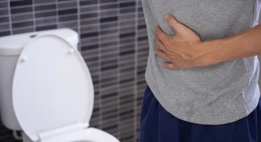 Mężczyzna trzyma się za brzuch, siedząc obok toalety. Może to być jeden z objawów raka odbytu.