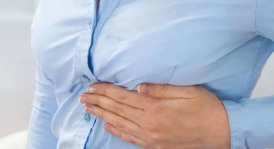 Kobieta trzyma się za bok, odczuwając ból pod lewym żebrem.