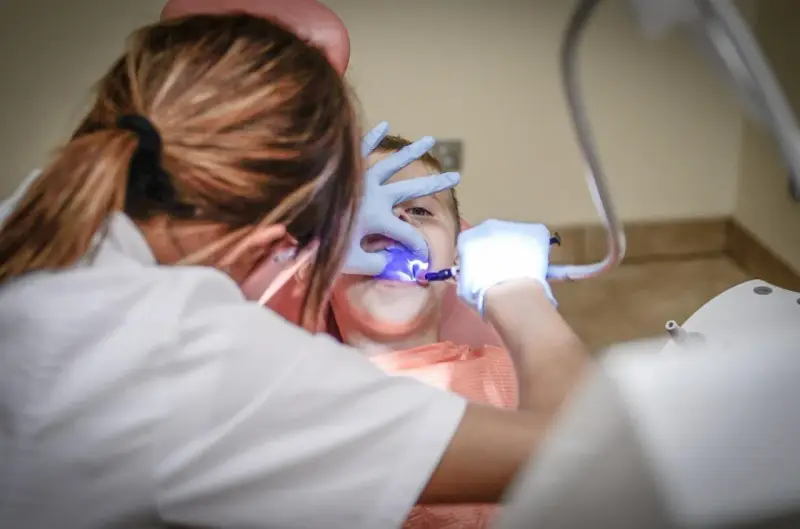 Dentysta w rękawiczkach bada zęby dziecka przy użyciu niebieskiego światła.