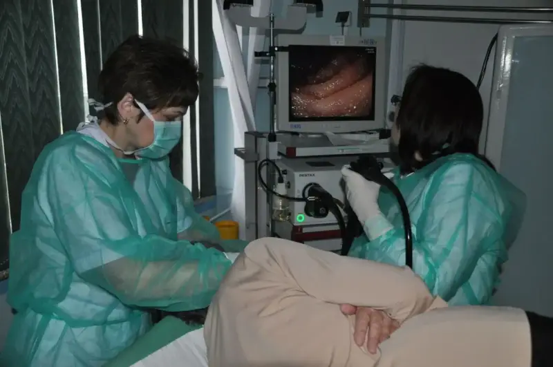 Lekarze w zielonych fartuchach przygotowują pacjenta do gastroskopii, obserwując obraz na monitorze.